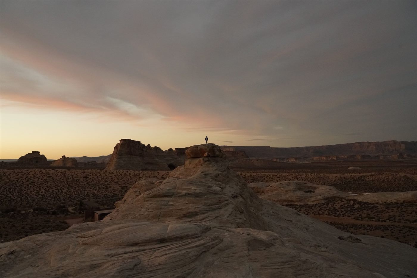A lone figure standing on a sandstone ridge in the Utah desert at dusk